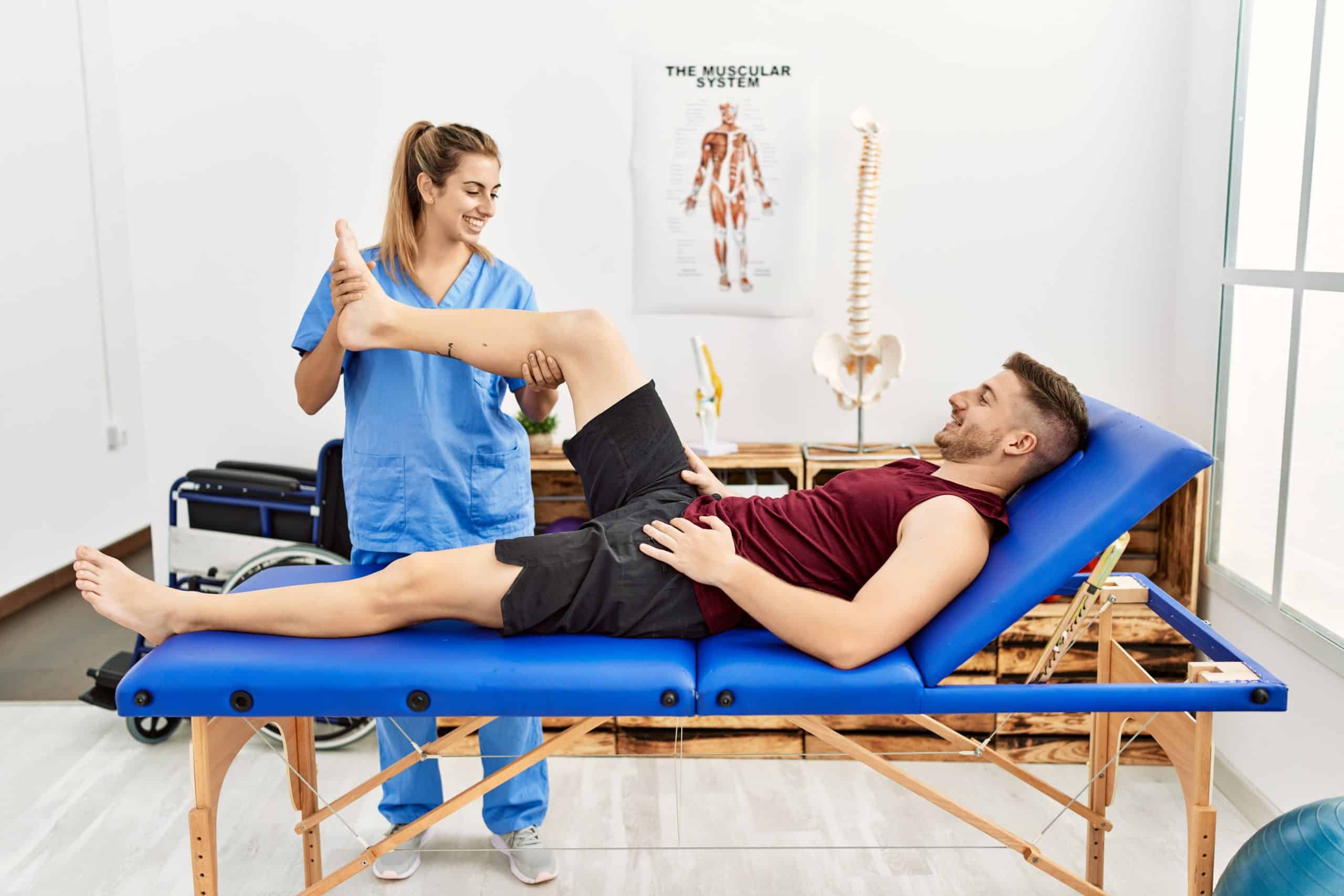 Young female physiotherapist treating male patient on treatment table.