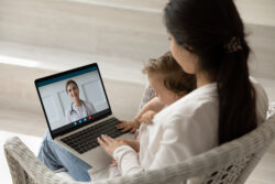 Loving mother hugging holding baby little daughter, using laptop, making video call to female pediatrician at home. These services should be included in the clinic marketing strategies for consideration.