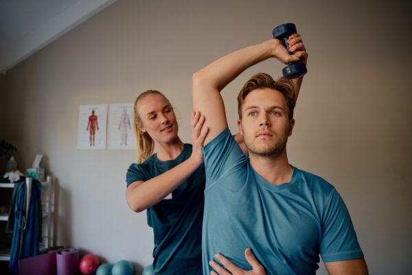 A therapist works with her patient on strength training with a dumbbell as part of rehabilitation therapy - one of the distinctive areas of sports physical therapy